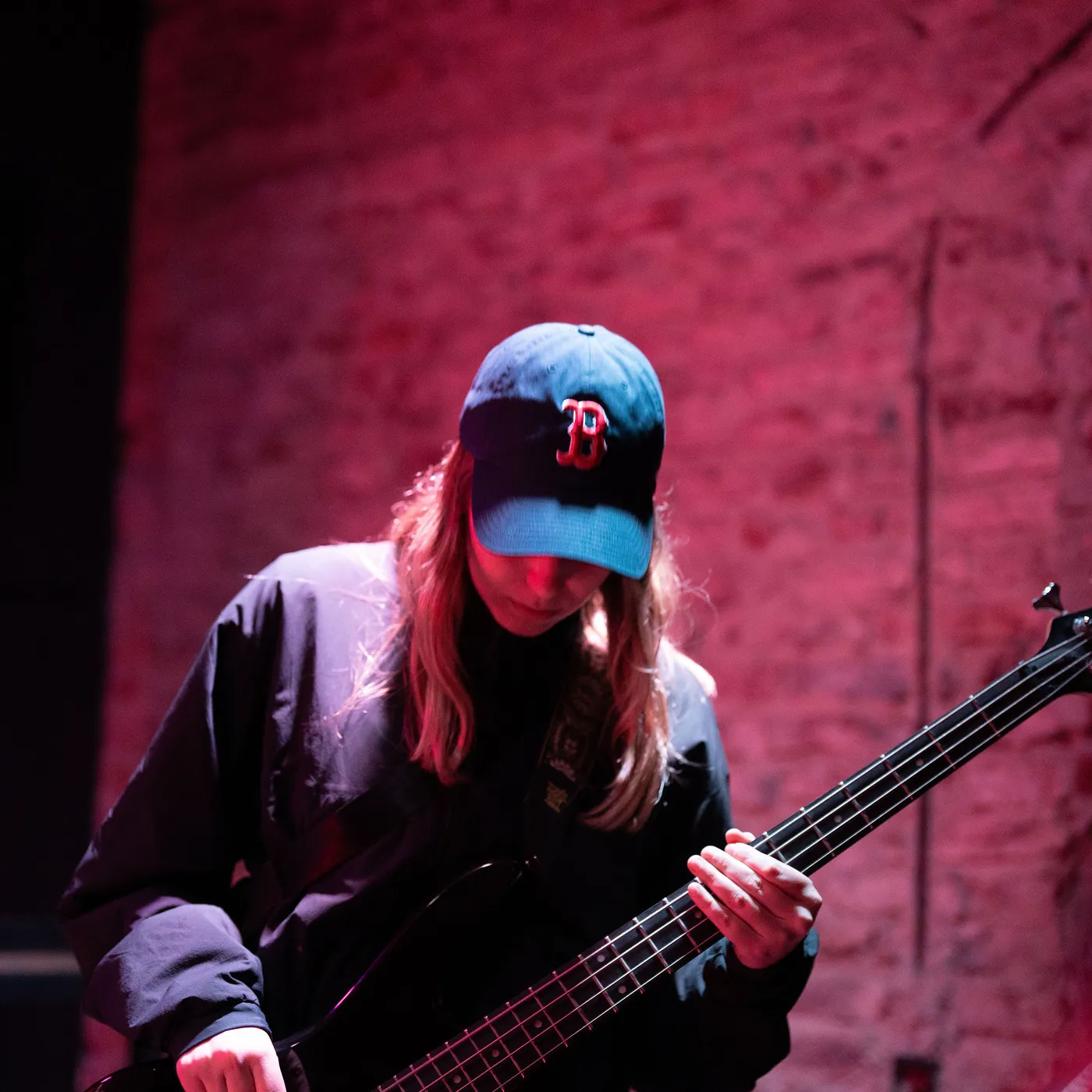 Julia playing bass in a Boston cap, under red light